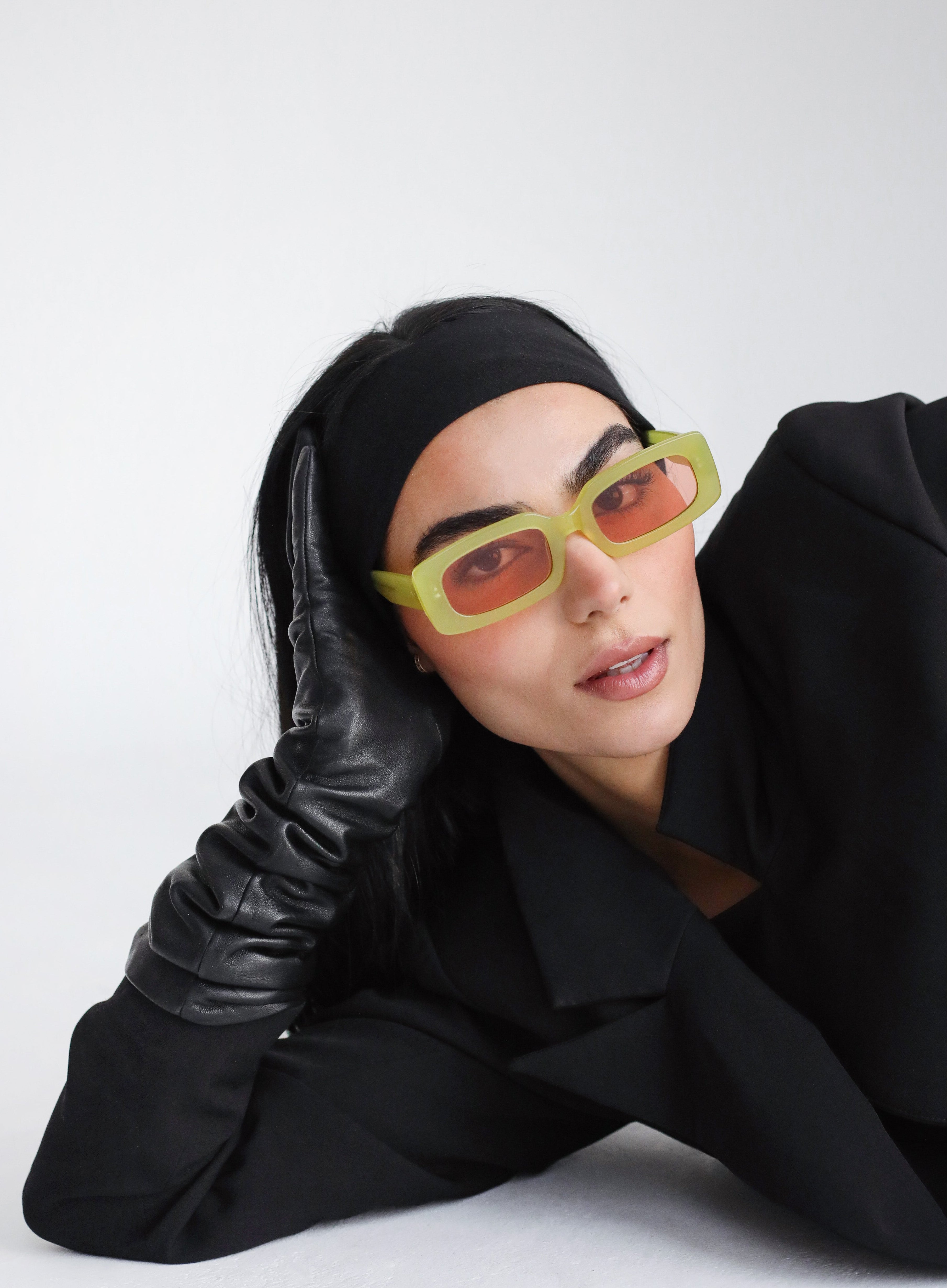 Person wearing a black outfit, black gloves, and yellow sunglasses with a white background