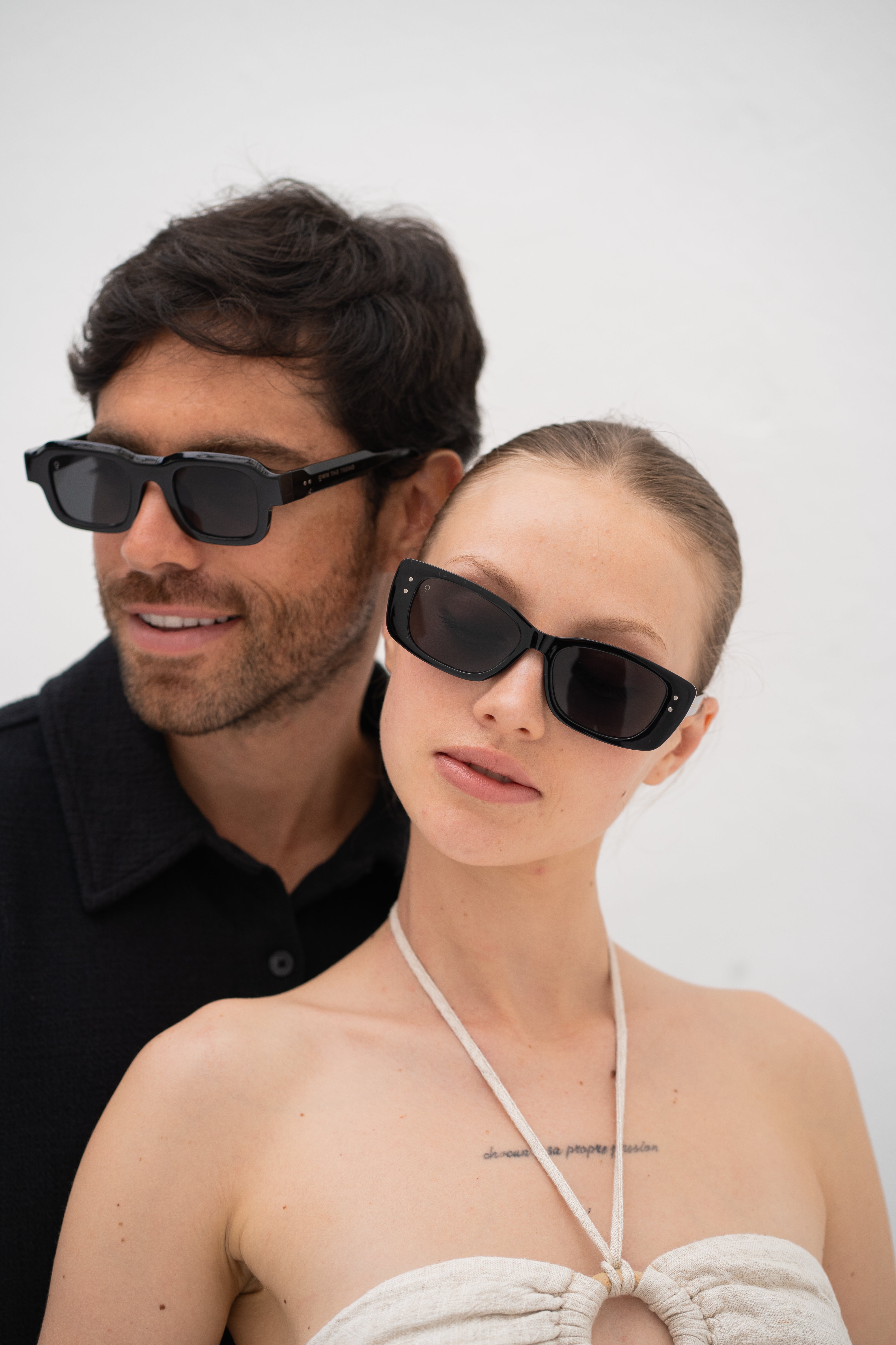 Man and woman wearing black sunglasses against a white background